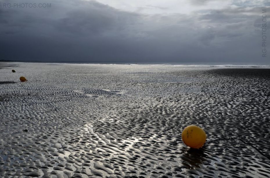 Trois bouées sur le sable à marée basse sous un ciel d'orage